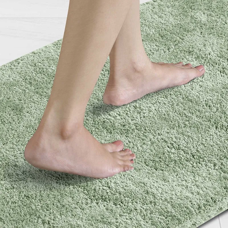 Bare feet standing on a light green plush bath mat