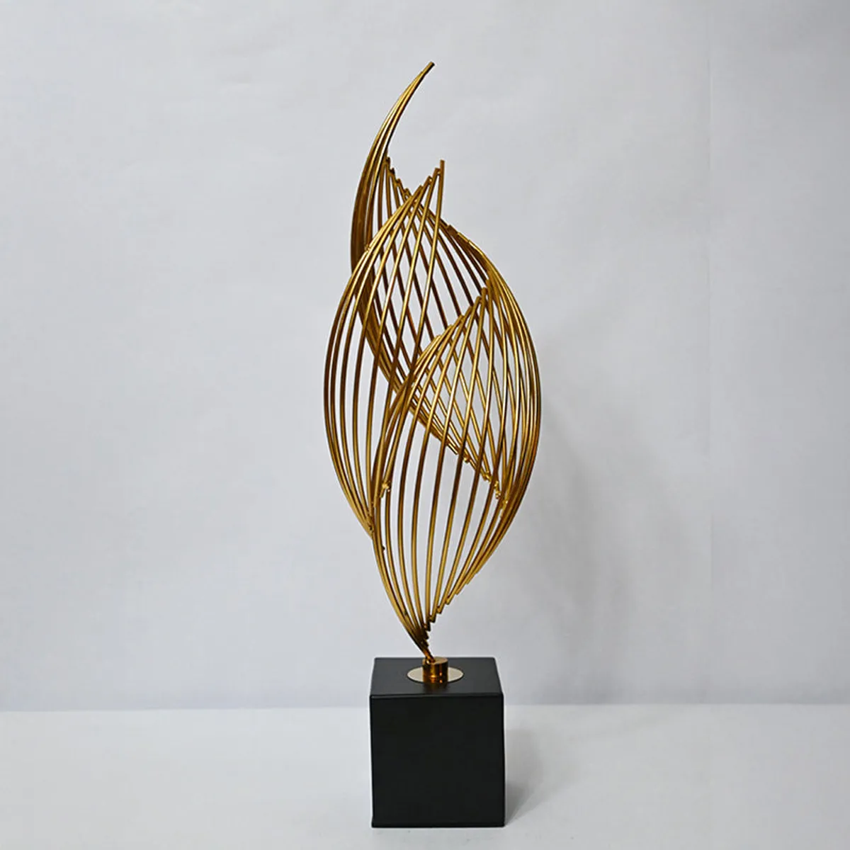 Gold abstract metal showpiece on a black base against a plain light backdrop