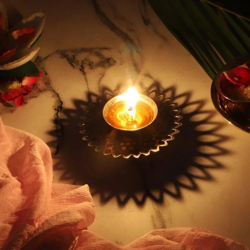 Lit brass diya casting decorative shadows on the surface