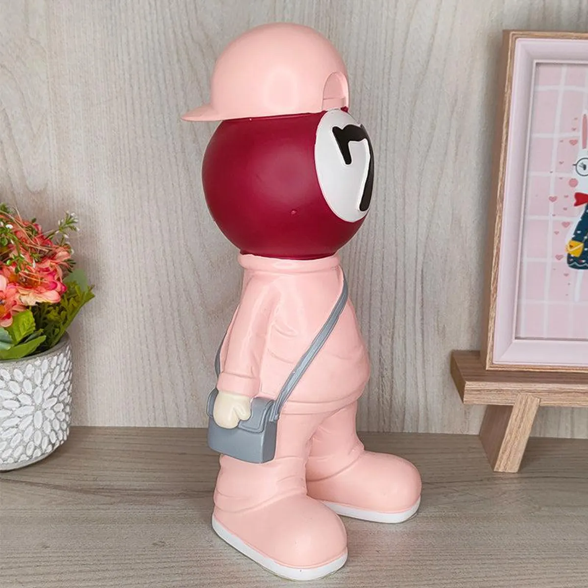 Angled side view of the pink billiards-ball figurine with a grey sling bag
