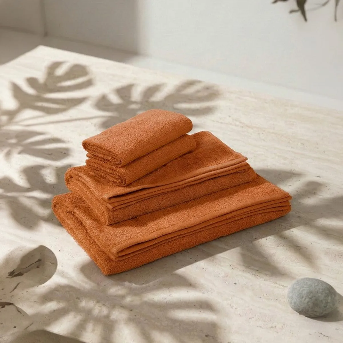 Stack of orange towels arranged on a light surface with leaf shadows