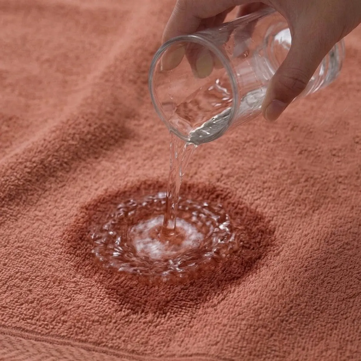 Water being poured onto the absorbent surface of a peach-brown towel