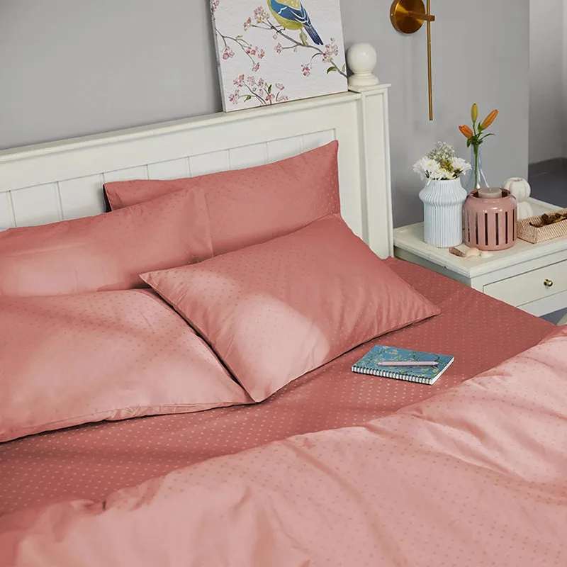 Pink-brown dotted bedding arranged on a white bed with cushions