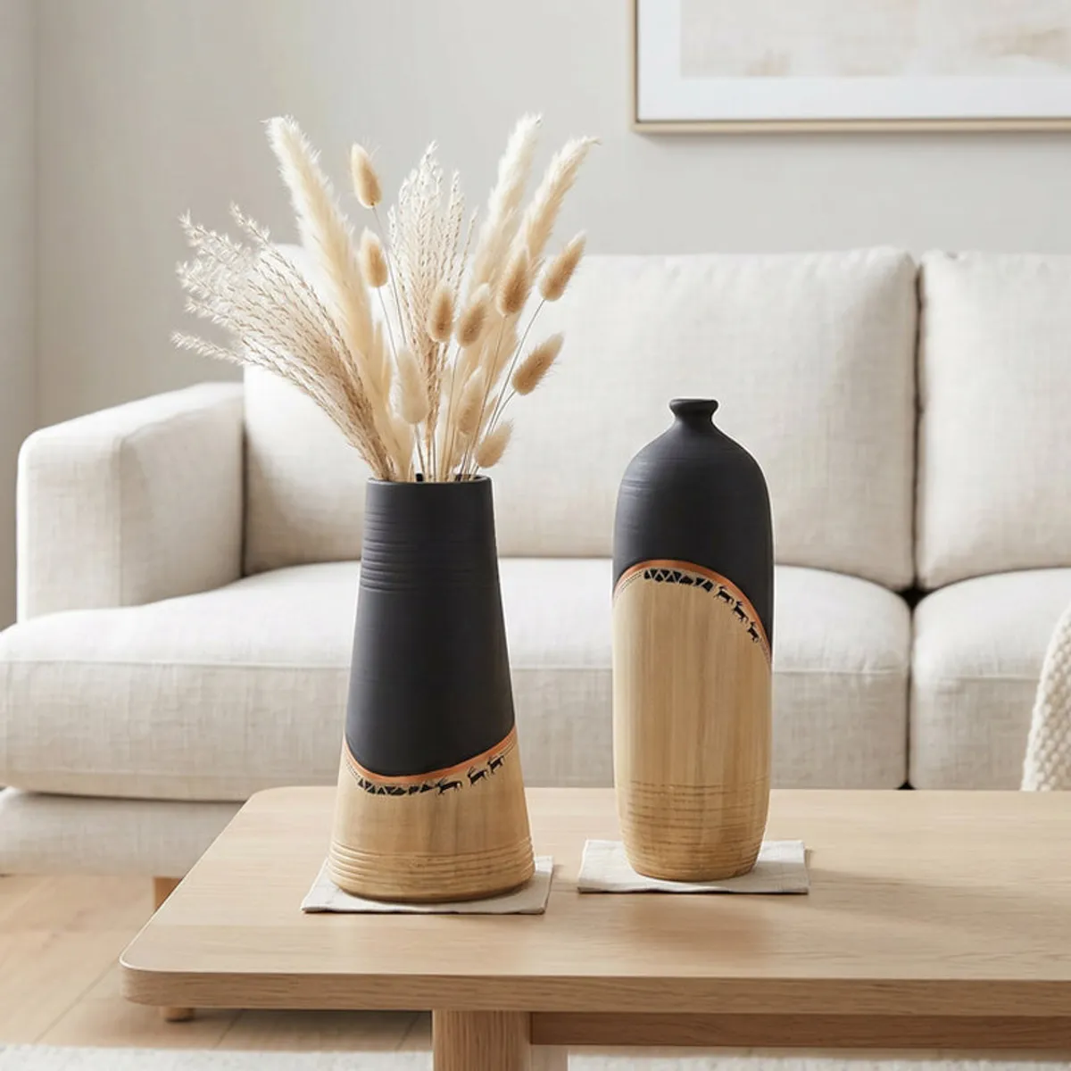 Two black and beige vases styled on a coffee table with dried stems