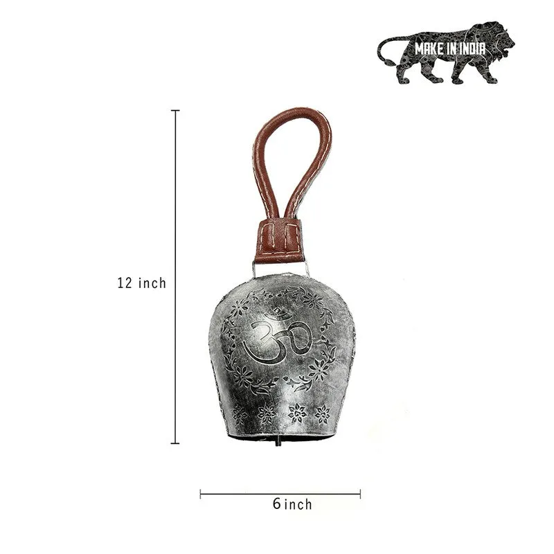 Silver decorative bell hanging outdoors among green foliage