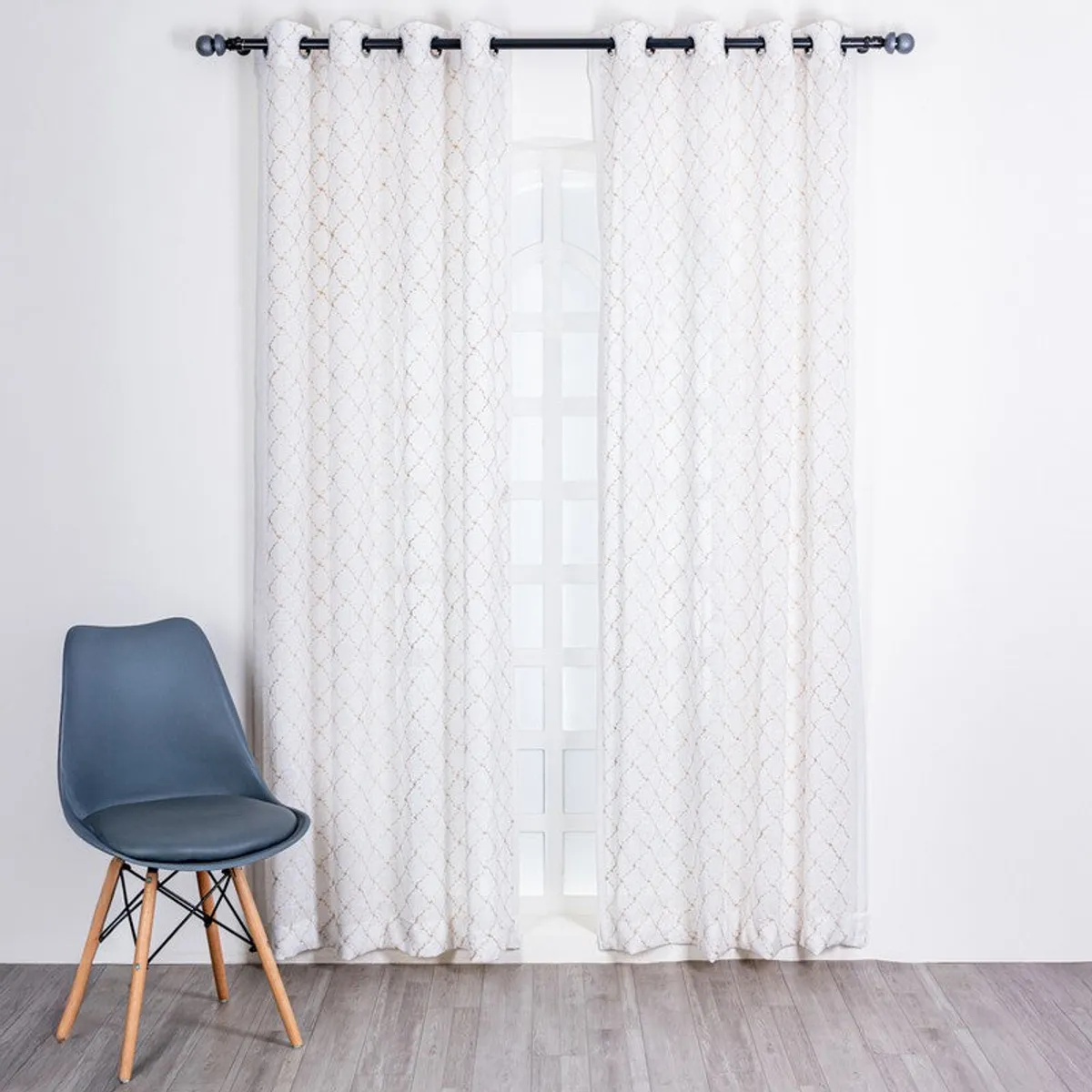 Pair of white sheer curtains with gold geometric embroidery on a window.