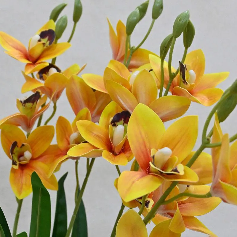 Close-up of yellow-orange artificial orchid blooms with green buds and leaves