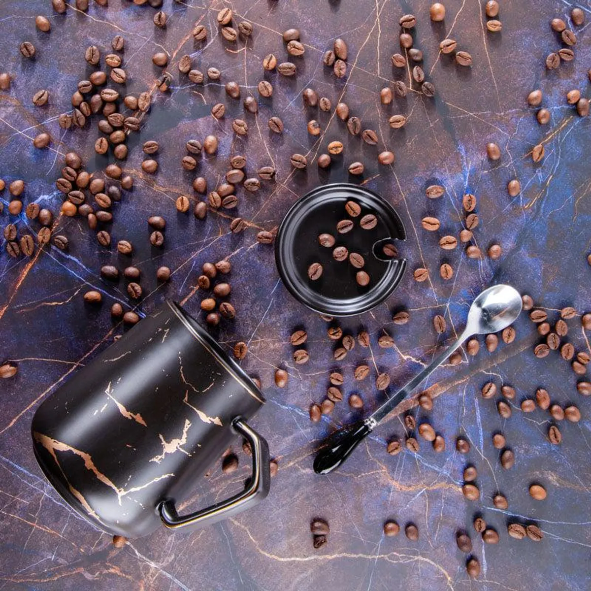 Black mug, spoon and lid arranged with coffee beans on a patterned surface