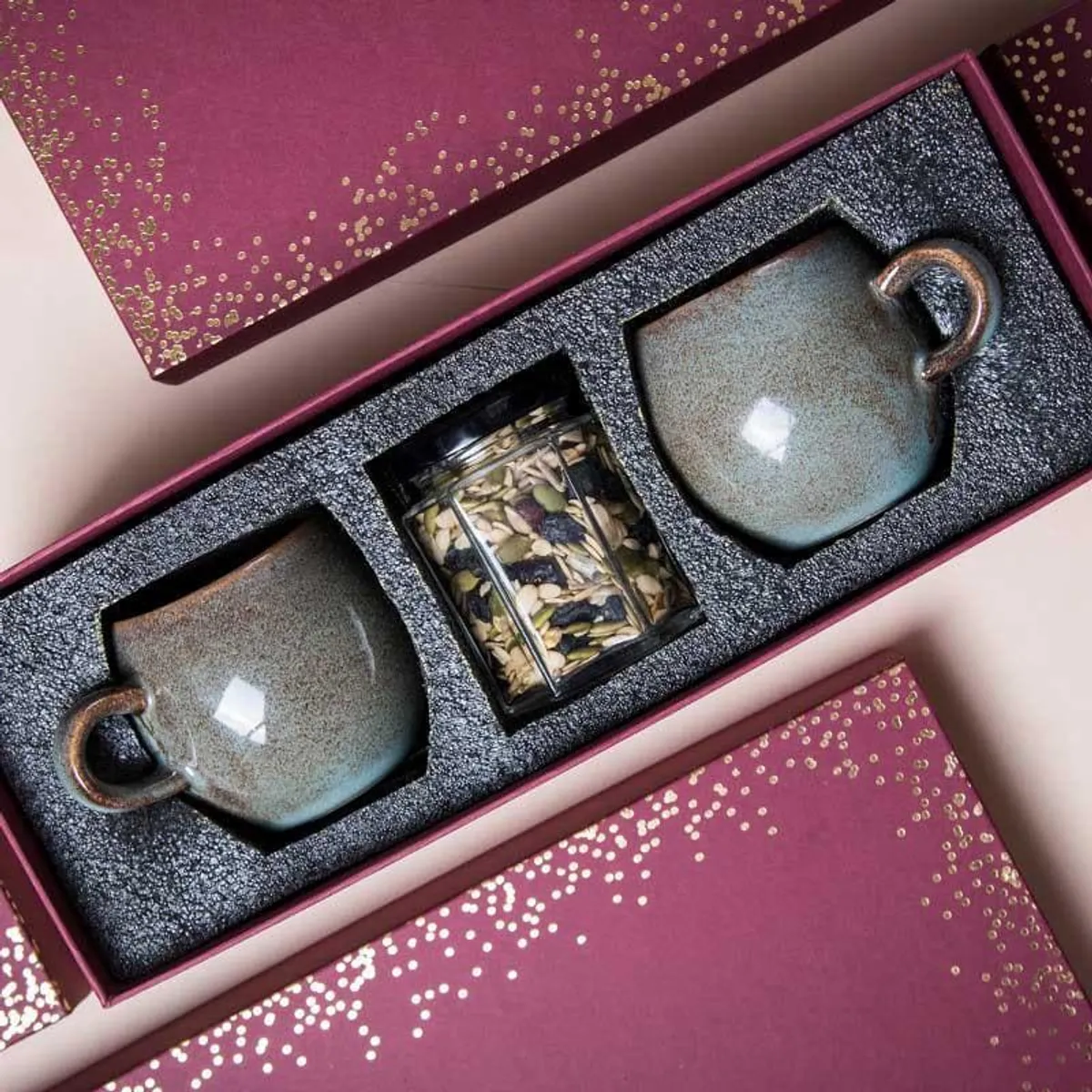 Open maroon gift box displaying grey mugs in fitted compartments