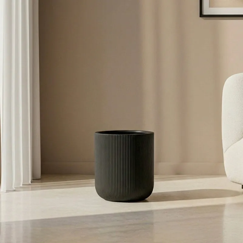 Empty black ribbed cylindrical planter on a sunlit living room floor.
