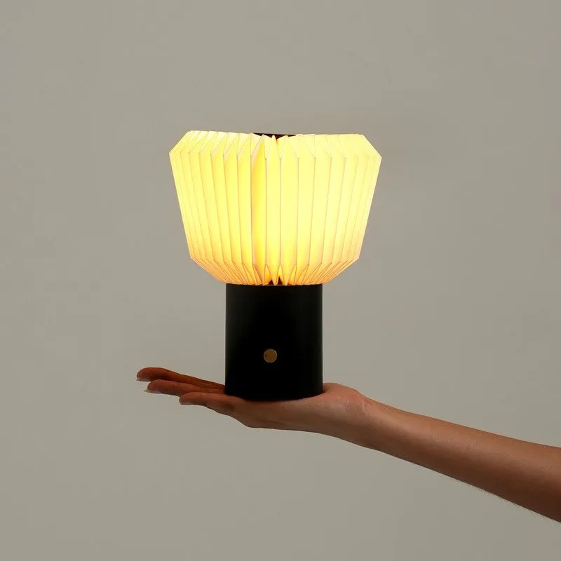 Glowing pleated table lamp balanced on a hand, showing its compact size
