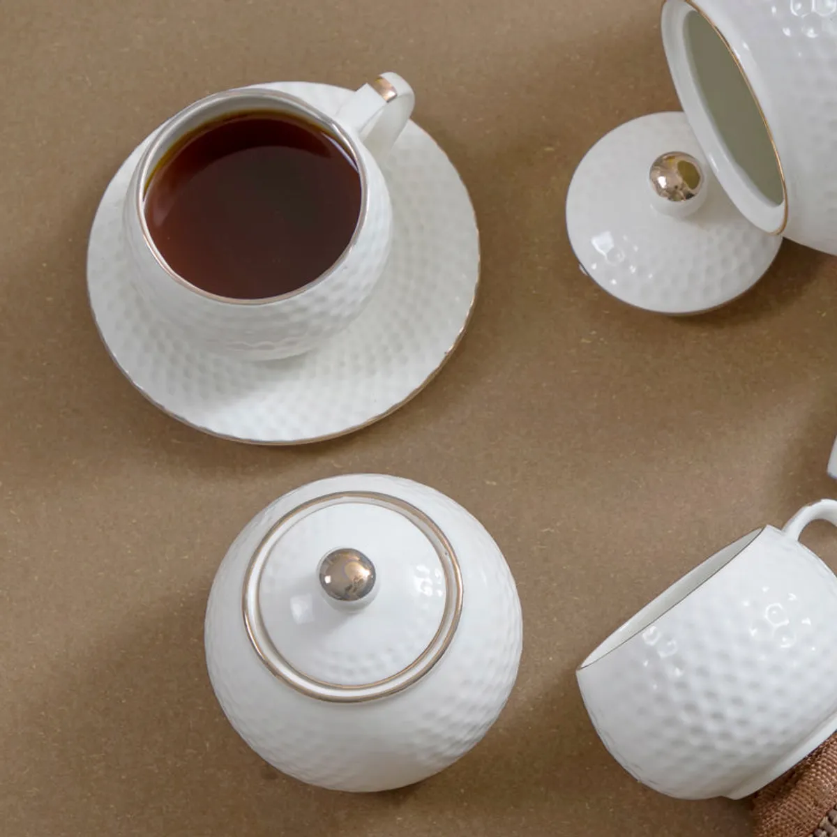 Close-up of a white textured teacup, saucer, teapot and sugarpot with gold accents