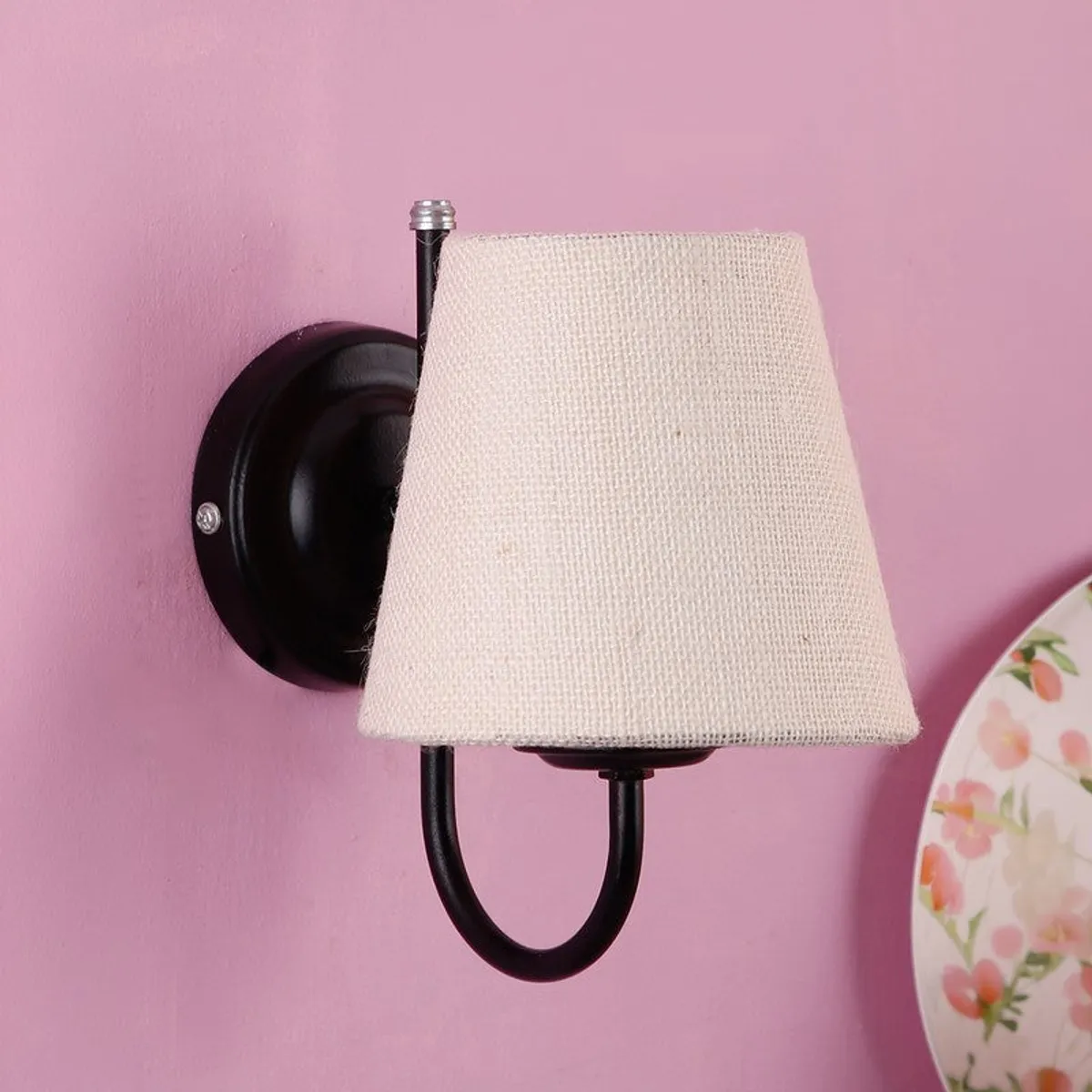 Off-white jute wall lamp with black iron base on a pink wall