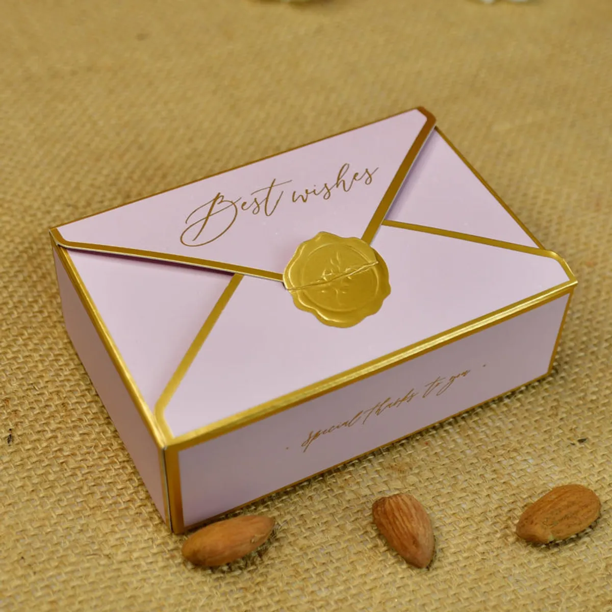 Pink gift box with gold edging, envelope-style lid and a gold seal.