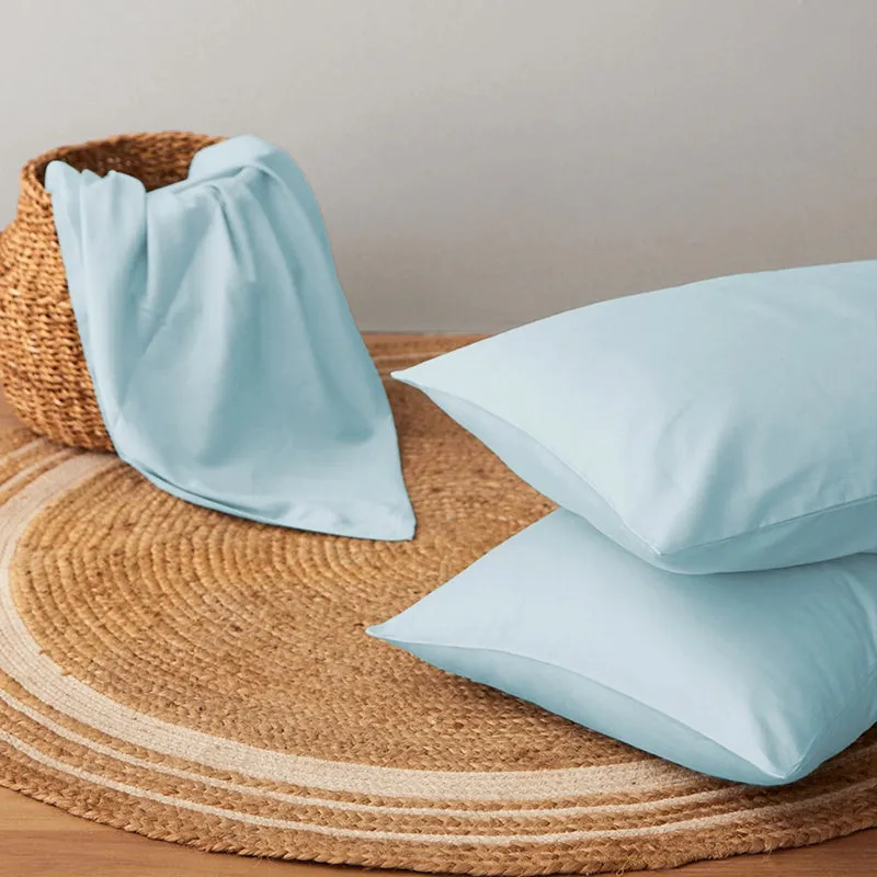 Pale blue pillow covers and bedding styled on a natural-fibre rug.