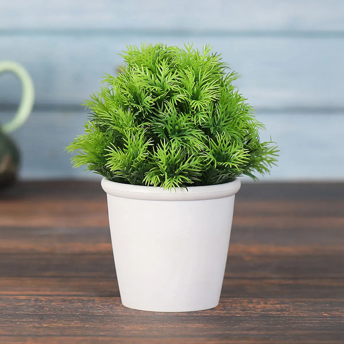 Single green artificial plant in a white pot on a wooden table