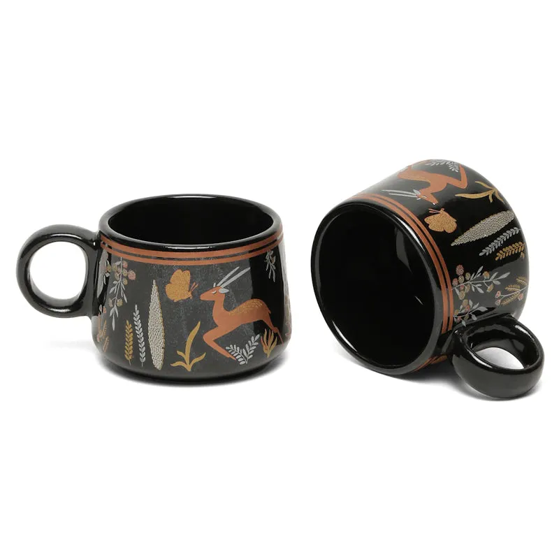 Close view of a black ceramic tea cup showing wildlife and botanical detailing