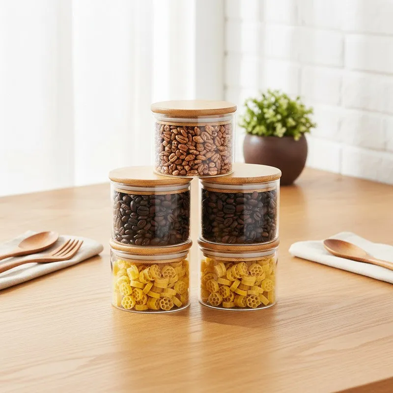 Five transparent glass jars with bamboo lids arranged on a wooden kitchen counter.