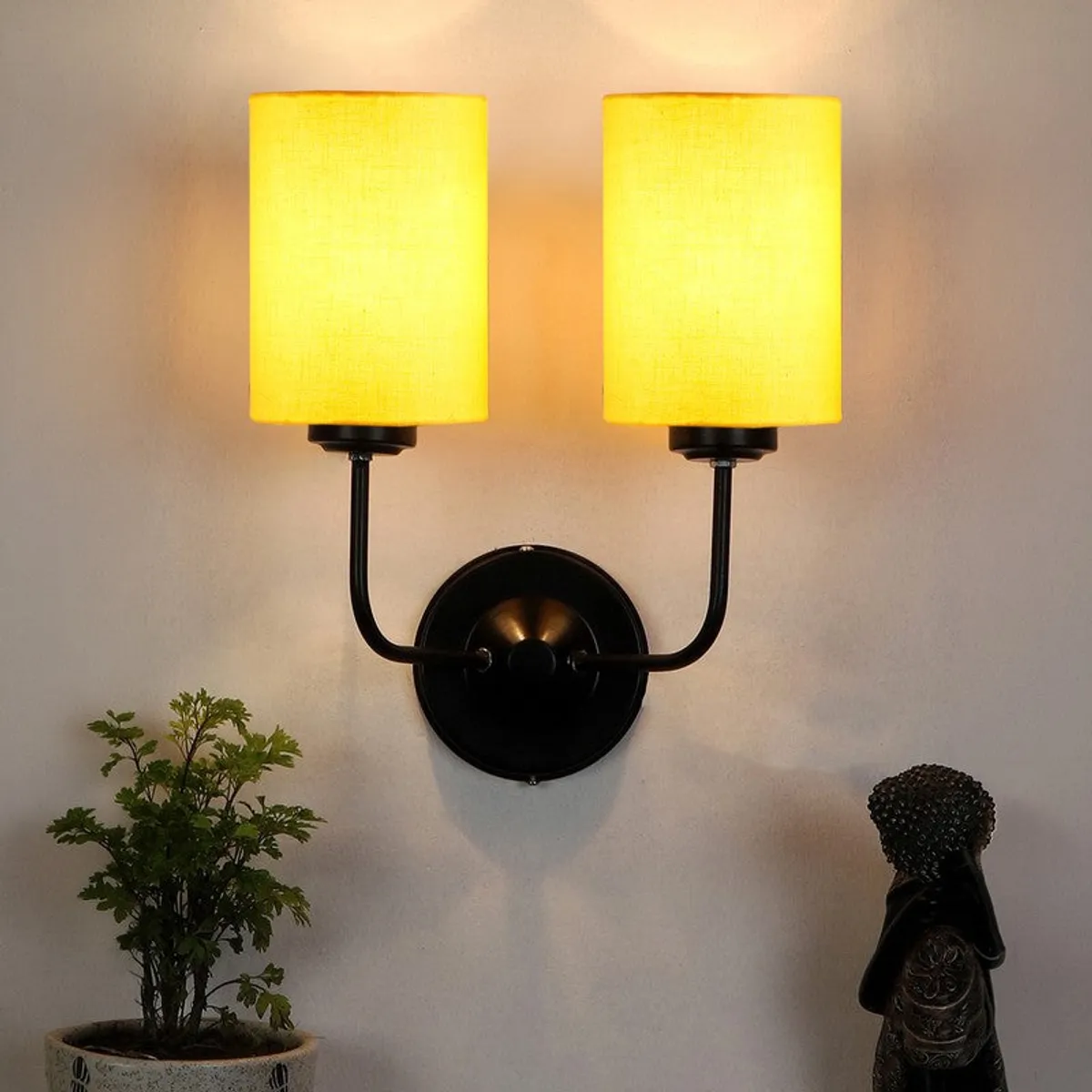 Lit yellow twin-shade wall lamp with black iron base on a wall