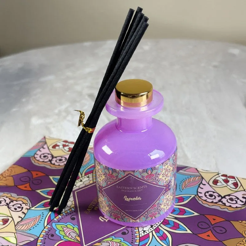 Purple glass diffuser with black reeds displayed on a colourful patterned box