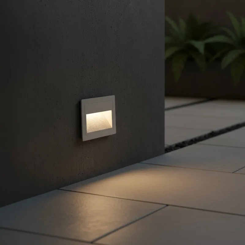 White recessed step light mounted low on a dark wall, casting a warm downward glow