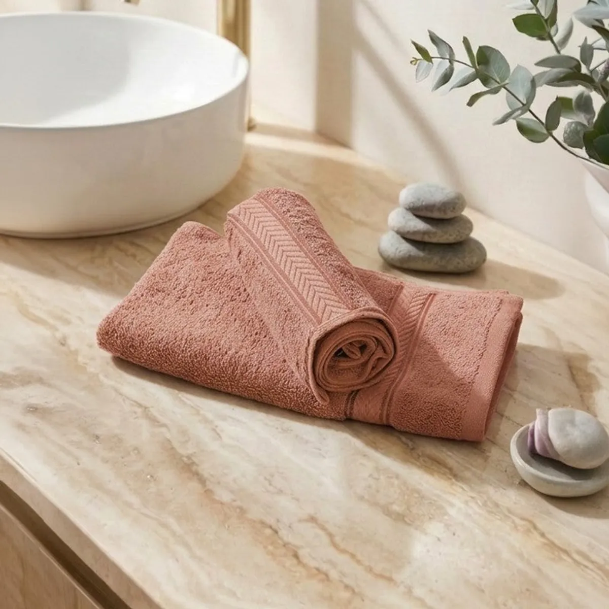 Folded peach-brown hand towels with patterned borders on a marble surface