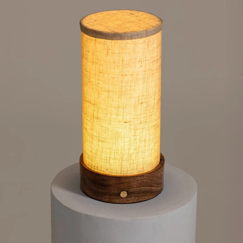 Lit beige touch lamp with wooden base on a white pedestal