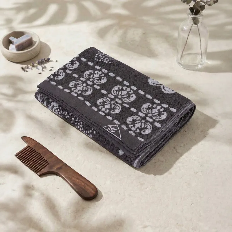 Folded grey bath towel with floral pattern on a soft neutral surface