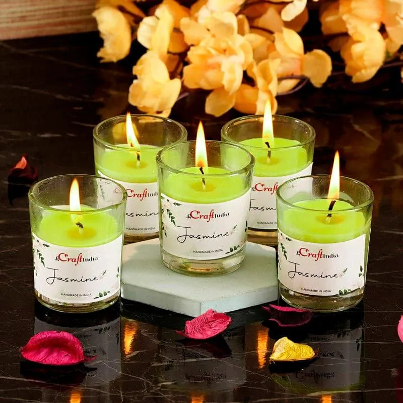 Five green jasmine candles in clear glass holders arranged on a dark surface
