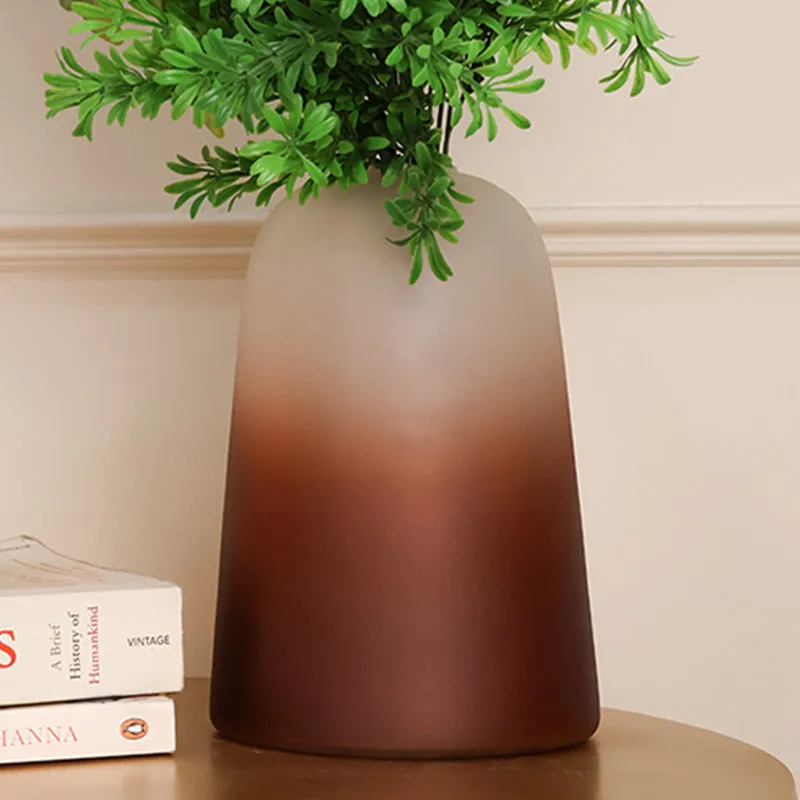 Front view of a tall frosted brown tapered glass vase with greenery
