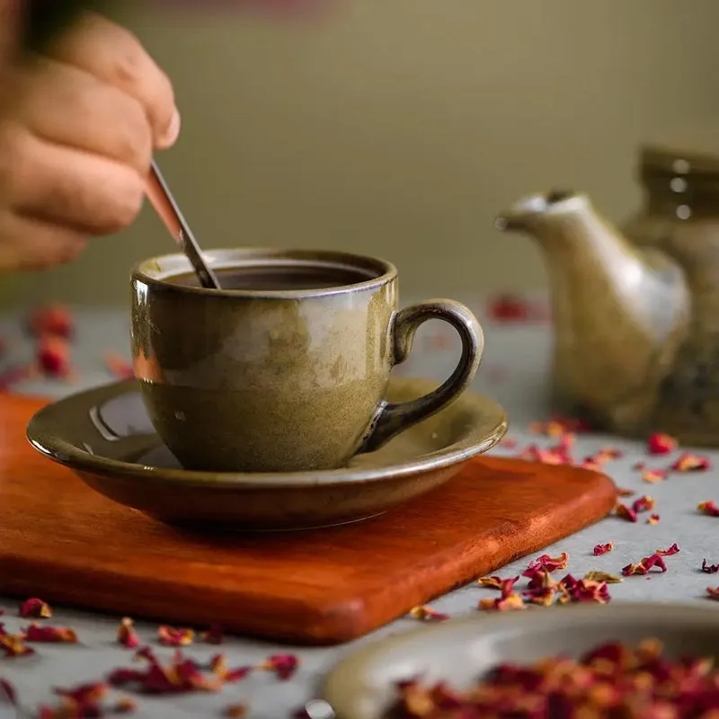 Green ceramic cup and saucer with teapot in the background
