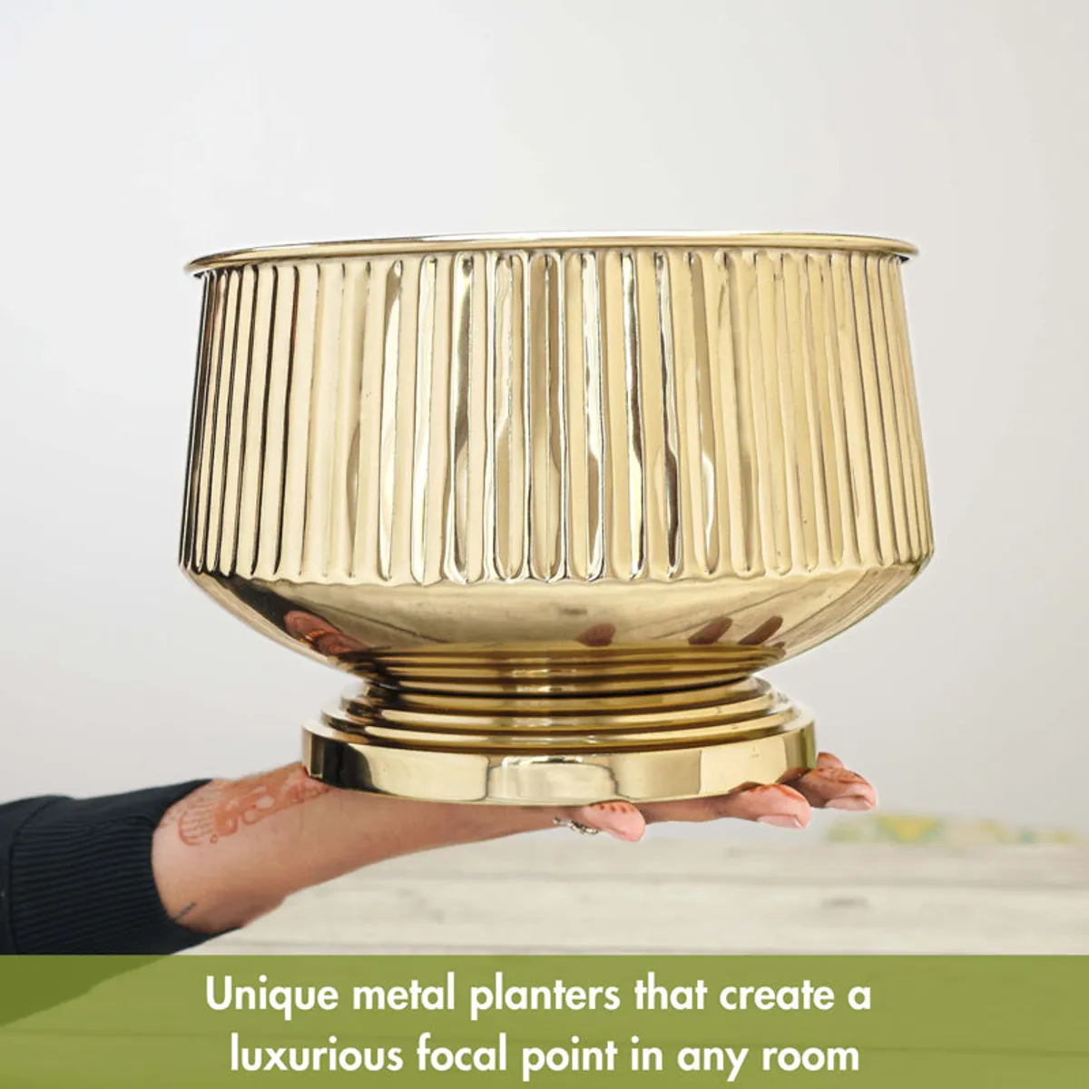 Gold cylindrical fluted planter shown being held to demonstrate its size.