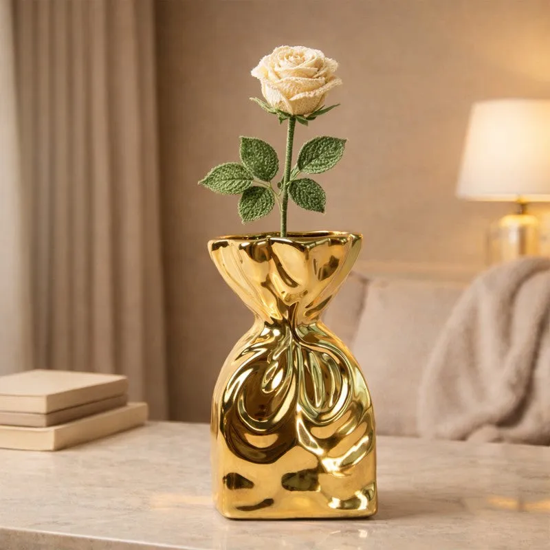 Gold sculptural vase with a single cream rose stem on a marble table