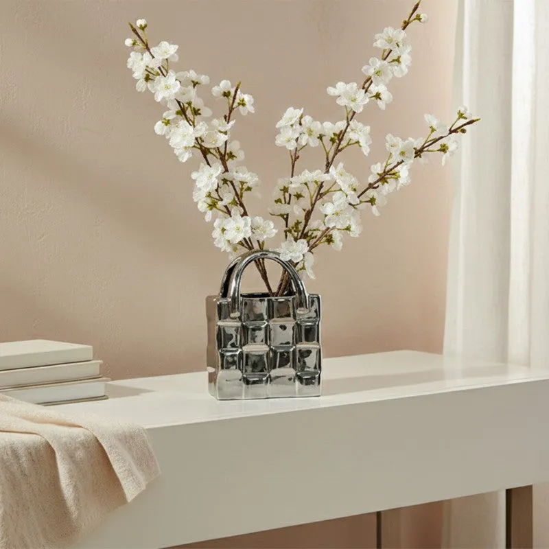Small silver handbag-shaped vase with white blossom branches on a console table