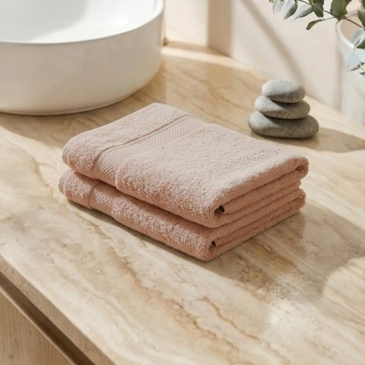 Two folded light beige hand towels on a marble bathroom counter.