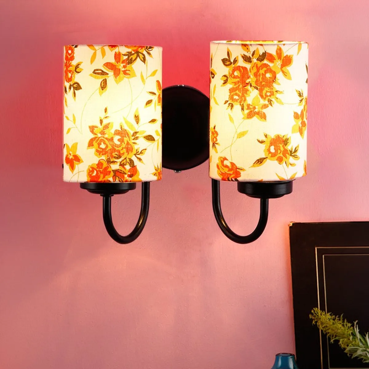 Close view of dual floral wall lamp with cylindrical shades on a pink wall