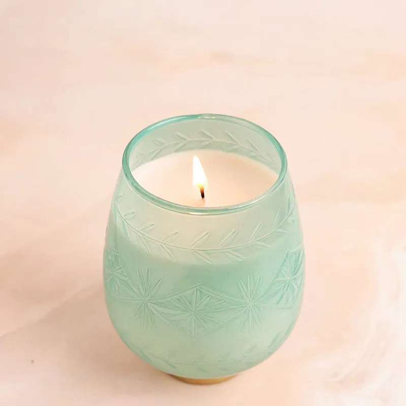 Lit green candle in a frosted patterned glass holder with a gold-toned base