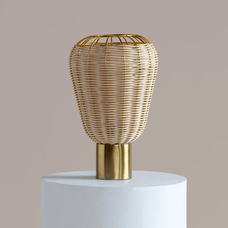 Beige rattan shade and gold base of a table lamp shown on a white pedestal