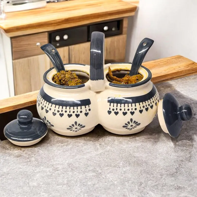 Open dual condiment jar with spoons on a kitchen counter.