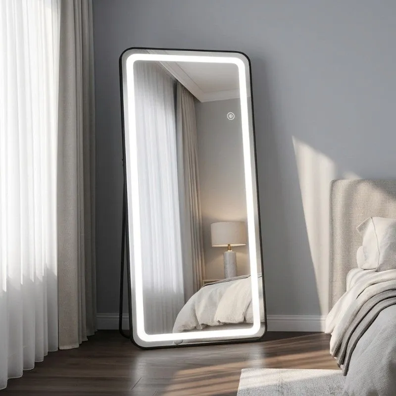 Full-length LED mirror with black frame standing beside a bright bedroom window.