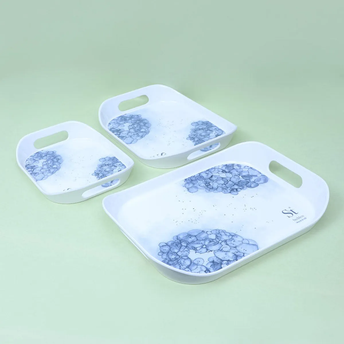 Three blue-and-white floral serving trays arranged separately on a green surface.