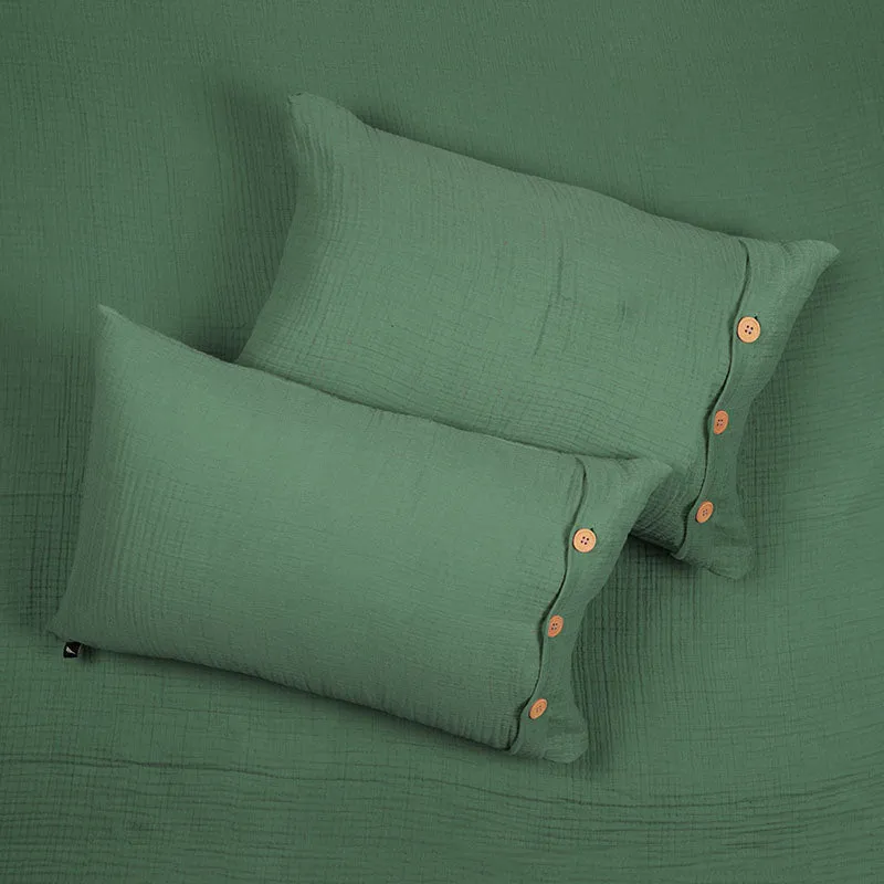 Two green pillow covers with button accents resting on the matching bedsheet