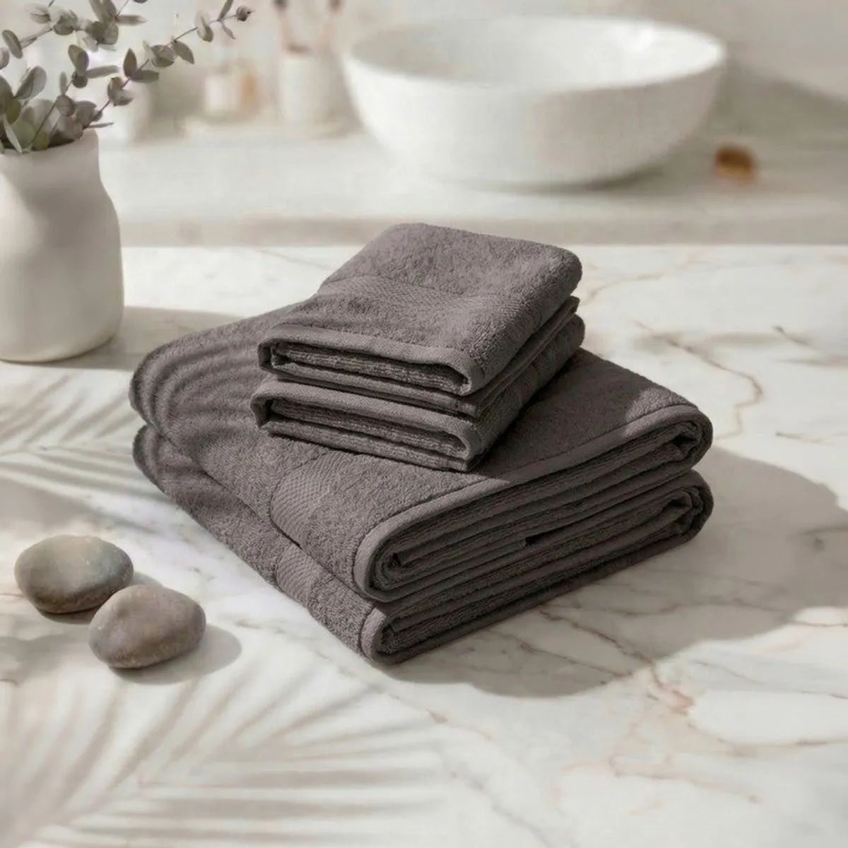 Folded grey towels stacked on a marble surface near a sink