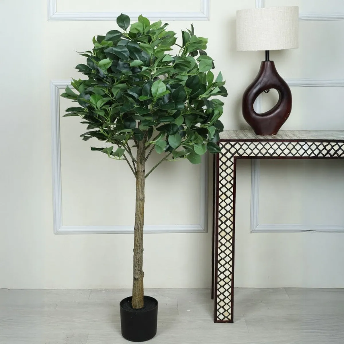 Green artificial camelia leaf topiary plant in a black pot beside a console table