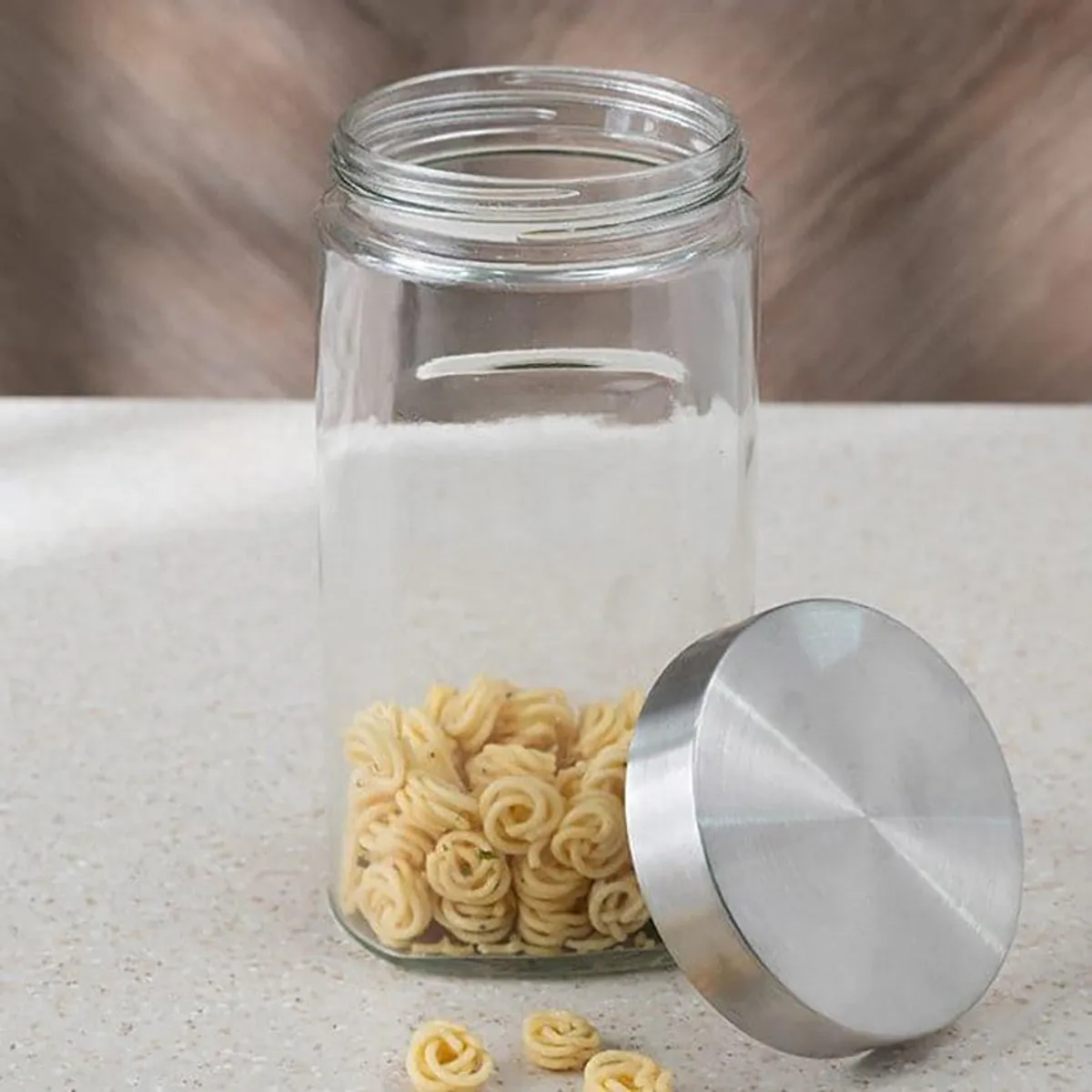 Open transparent glass container with its silver metal lid placed beside it.