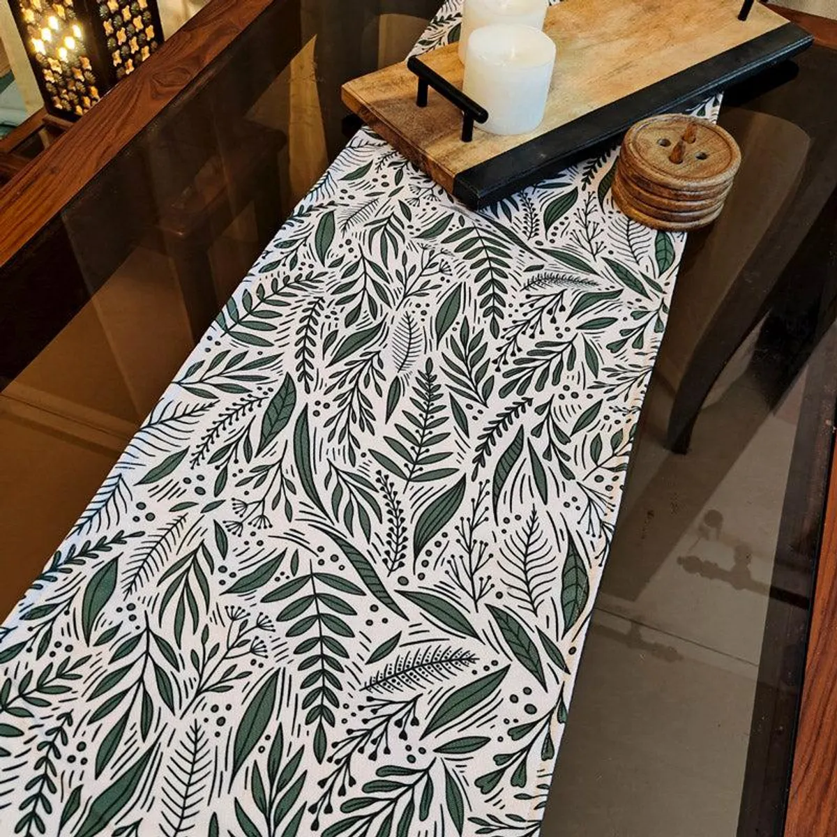Green and white leafy table runner styled with wooden trays and candles