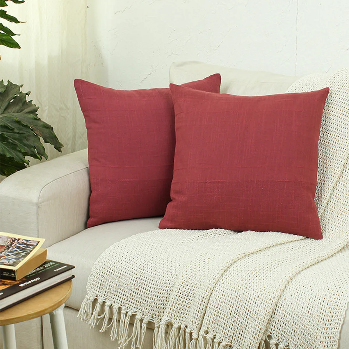 Two red square cushion covers styled on a light sofa with a cream throw