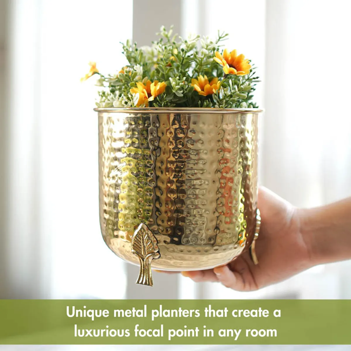 Hand holding a gold hammered metal planter with leaf-shaped legs