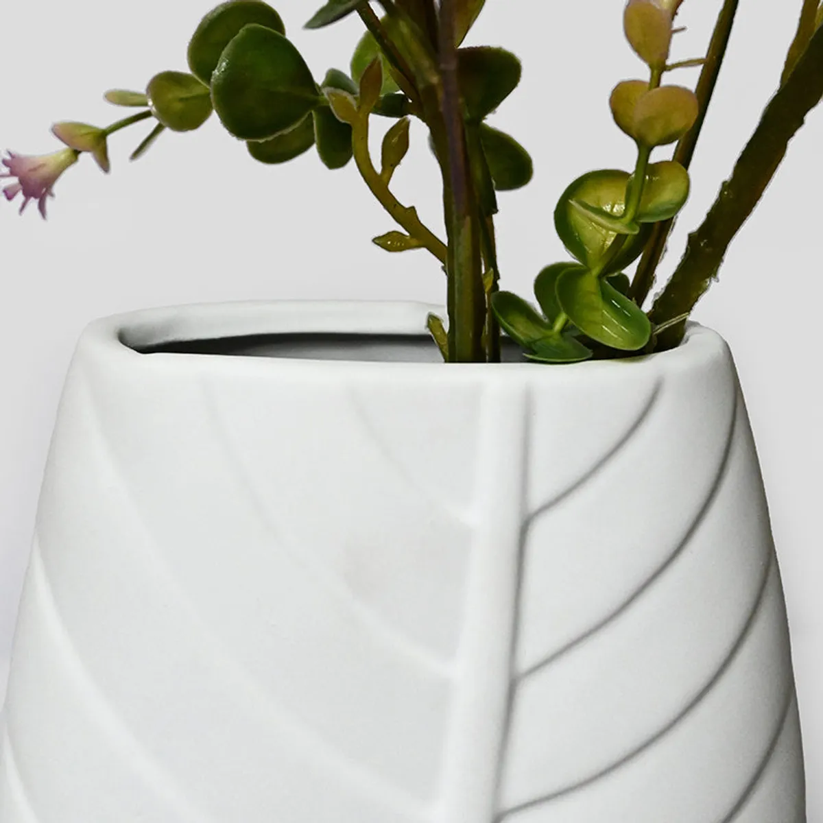 Close-up of the white vase with leafy embossed detailing and stems inside