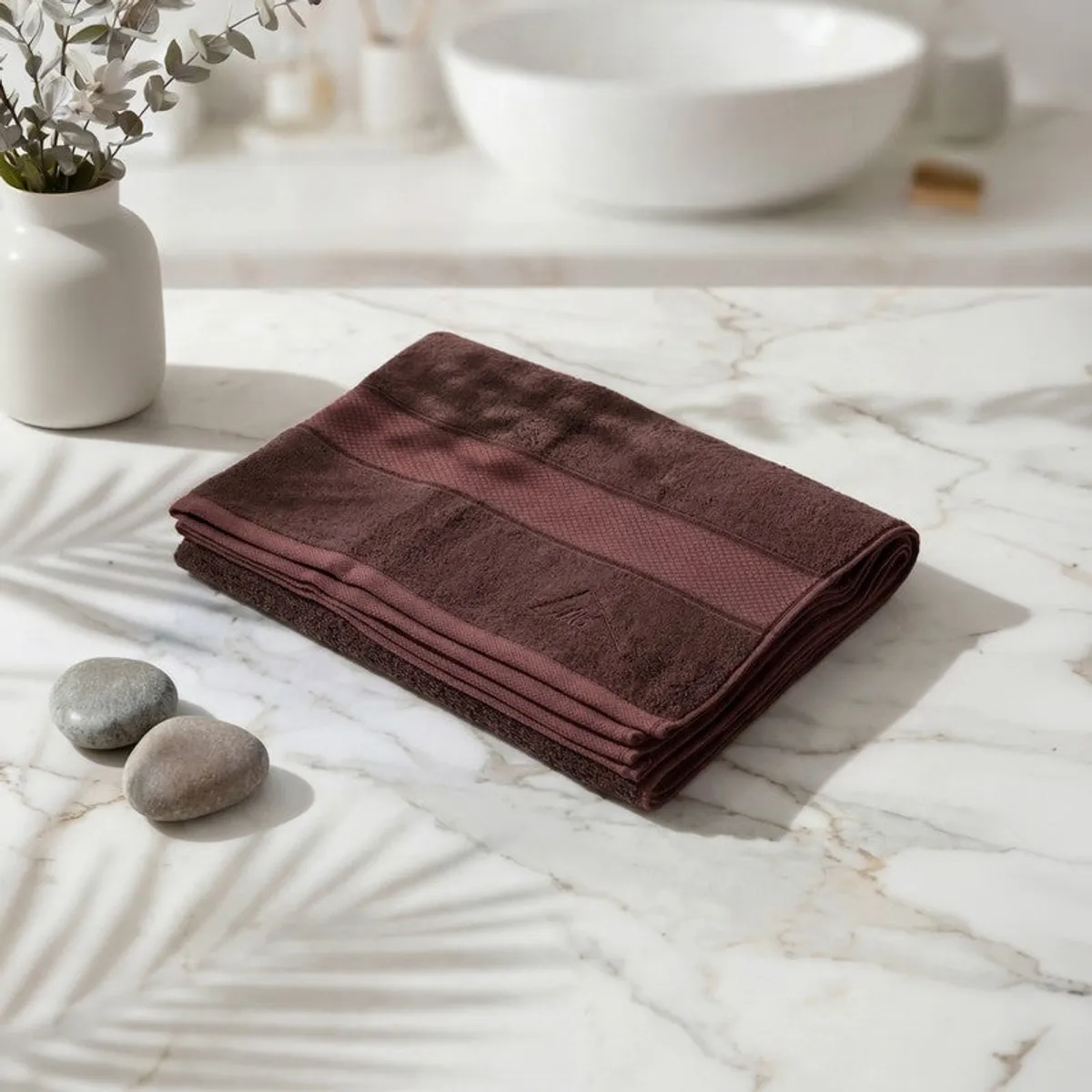 Folded coffee brown bath towel displayed on a marble bathroom counter.